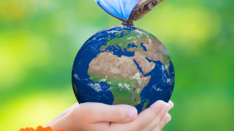 Child holding Earth planet with blue butterfly in hands against green spring