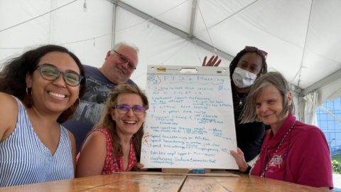 Five Employment team members sitting around a table smiling, with planning notes on flip chart paper in the middle of the table