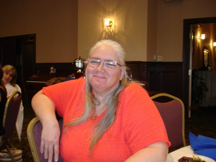 Diane is smiling at the camera. Background appears to be a hotel conference room. Michelle is peeking in the background.