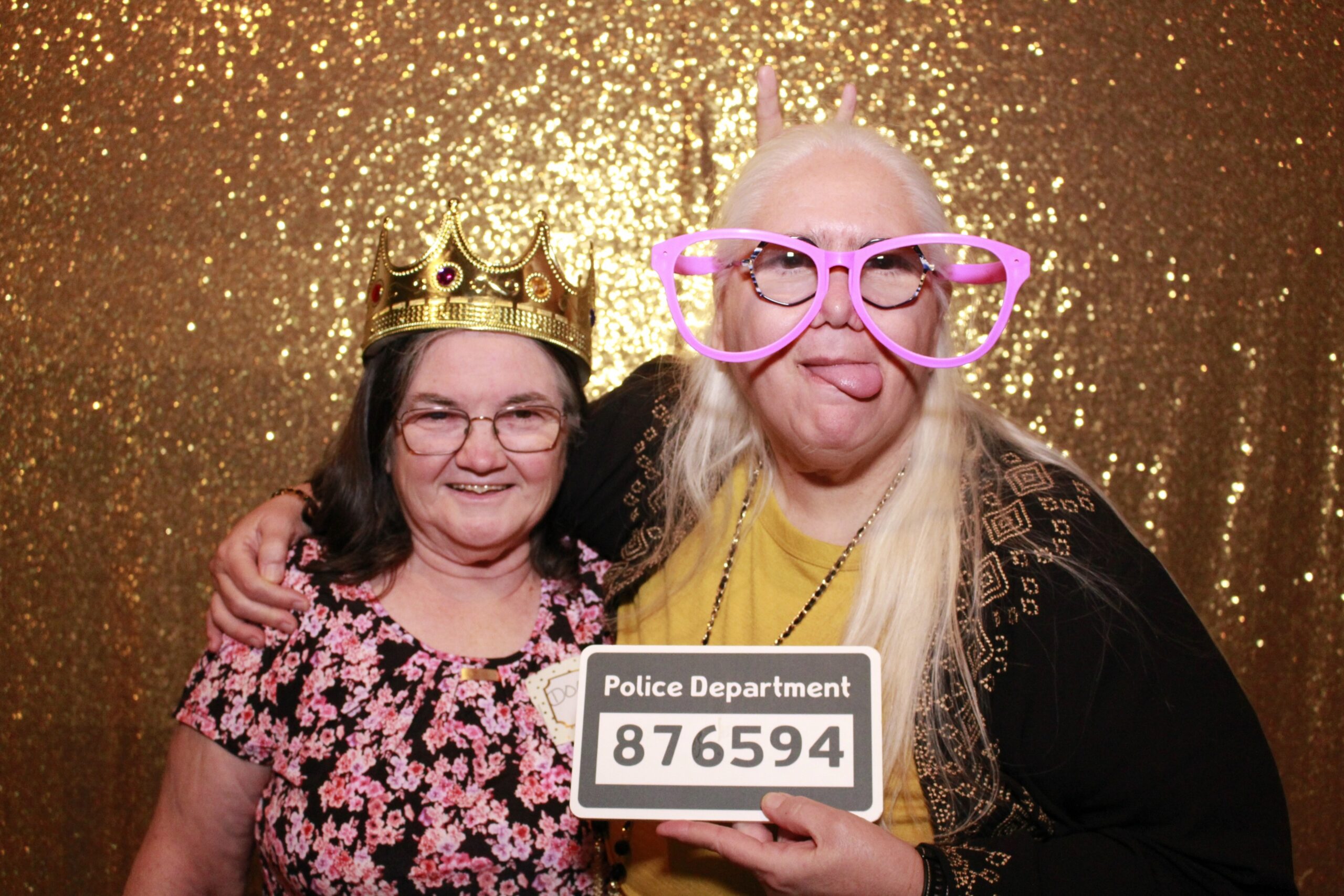 Diane and Doris posing. Doris is wearing a tiara, and Diane is wearing silly glasses holding a sign that says “Police Department #”