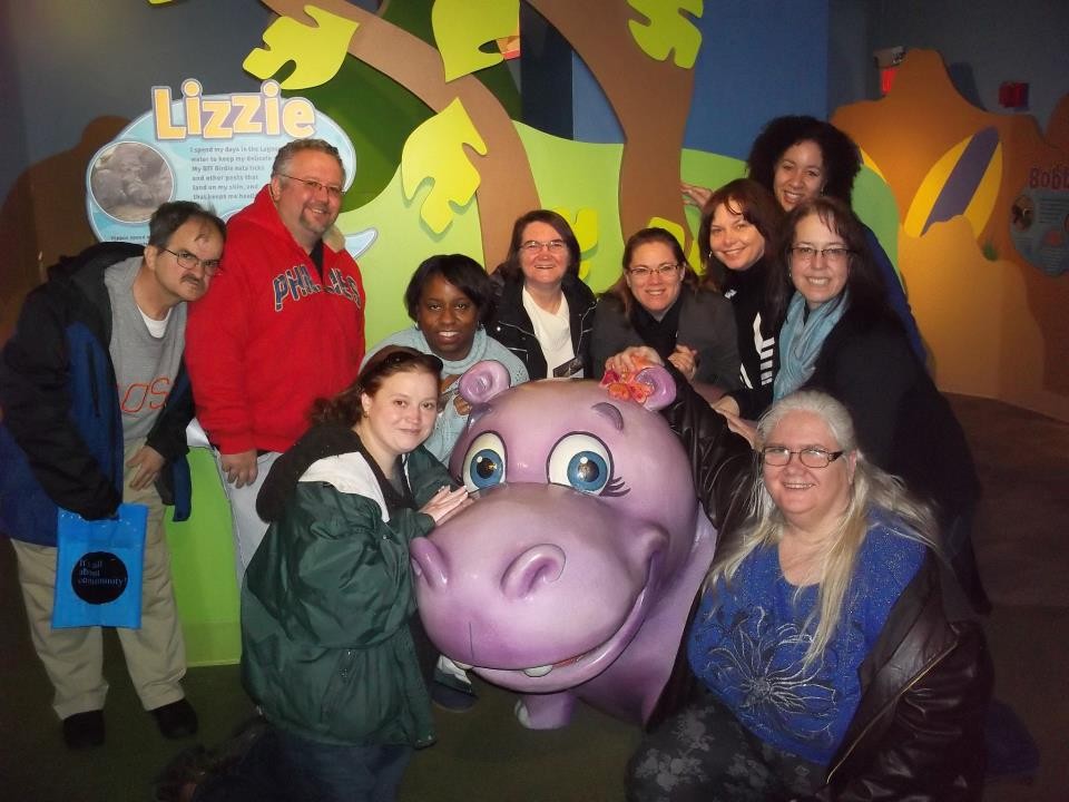 George, Joe, Stacey, Shauna, Jill, Julie, Tracy, Gerry and Diane taking a group shot with a pink hippopotamus at the aquarium.